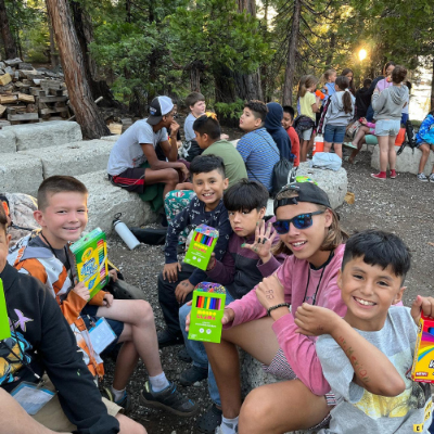 Children sitting outside near large trees, holding markers and showing artwork they've drawn on themselves with them.