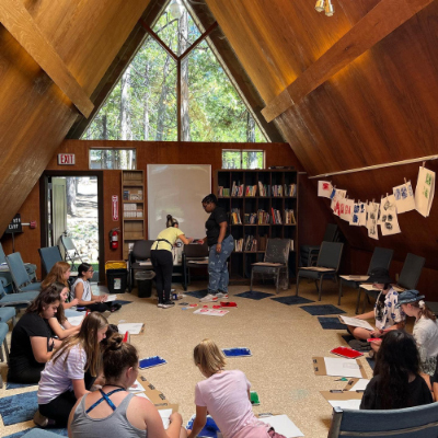 Children in a cabin sitting on the floor using paint and sponges to create artwork.
